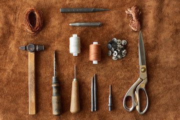 Artisan tools for working with leather: hammer, scissors, thick thread, metal wire, awl, buttons top view on leather background