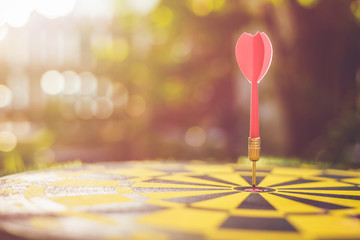 Red dart arrow in the center of dartboard. Blur and bokeh in sunrise time background
