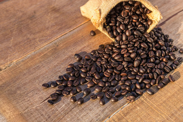 Roasted coffee beans in small sack on wooden table. Outdoor shooting with sunlight and blur background
