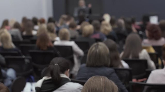 Many people at the conference listen to the presenter. Rear view of people sitting in the auditorium