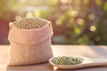 Mung beans in small wooden sack on wooden table. Outdoor shooting with sunlight and green blur bokeh and lens flare effect background