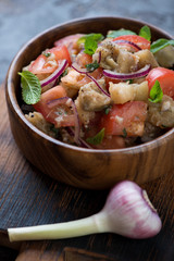 Close-up of a wooden bowl with baked eggplants and fresh tomatoes salad, vertical shot