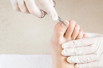 Hands in gloves cares foot nails. Pedicure beauty salon. Foot fingernails cutting with scissors.