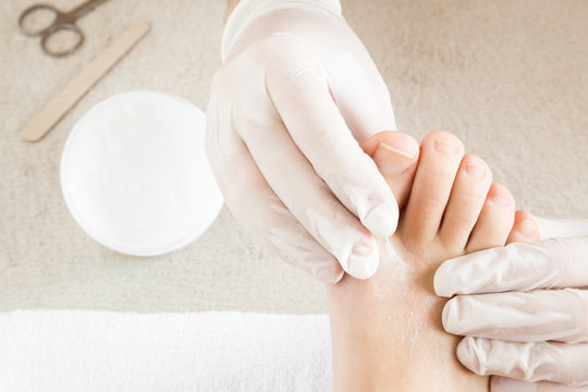 Hands in gloves cares foot nails. Pedicure beauty salon. Foot moisturizing cream.