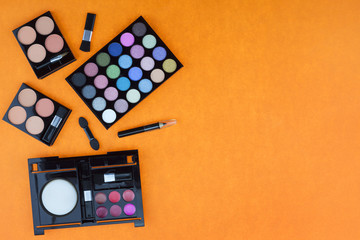 Flat lay photo of various makeup brush, eyeshadow and cosmetics on colorful paper background.