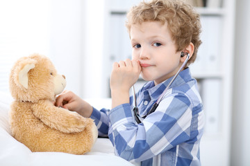 Child  patient afrer health exam playing as a doctor with stethoscope and teddy bear.