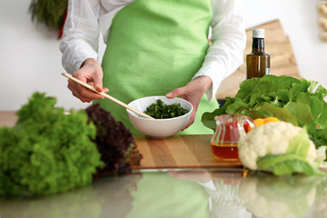 Closeup of human hands cooking vegetables salad in kitchen on the glass table with reflection. Healthy meal and vegetarian concept