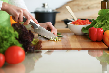 Closeup of human hands cooking vegetables salad in kitchen on the glass table with reflection. Healthy meal and vegetarian concept