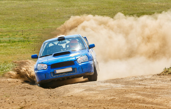 A blue rally car rides along a dusty road