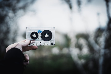 A man holds in his hand an old cassette tape with a flower inside against the sky and trees. Concept: nostalgic time.