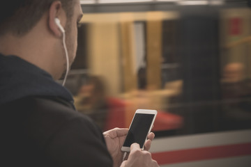 Urban man using smartphone and earphones at the train station 