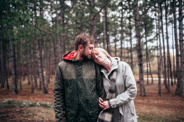 A loving guy with a girl is walking through the woods in the rain.