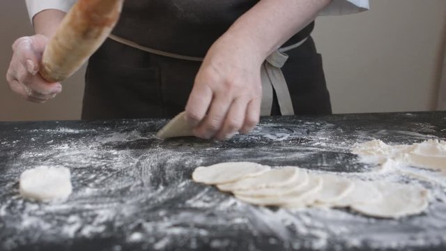 Two woman's hands making meat dumpling with wooden rolling pin.