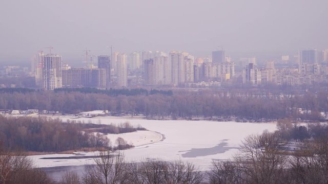 The city is on the bank of a frozen river. On the shore are visible buildings and building cranes. Kiev, Ukraine