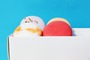 Tasty different colored macarons in white box on blue background