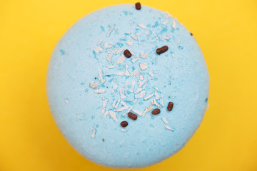 Blue macaron with coconut shavings and chocolate on yellow background.