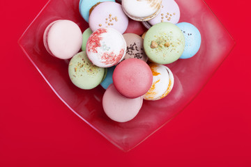 Tasty different colored macarons in  dish  on red background.