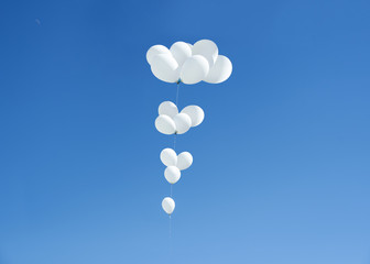 Imagen minimalista de un montón de globos blancos sobre un cielo azul despejado.
