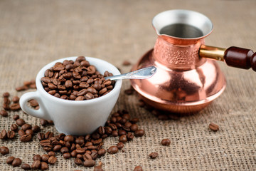 Cup full of coffee beans with turkish cezve on the cloth sack background