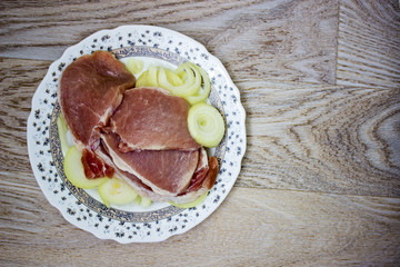 Escalope raw meat and onions rings, chop, ready for frying. On a wooden textured surface