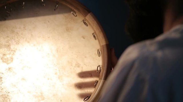 close up shot of man drumming out a beat on an arabic percussion drum named Dayereh at home. Shot at counterlight.