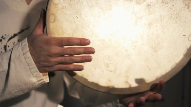shot of man drumming out a beat on an arabic percussion drum named Dayereh at home. Shot at counterlight.