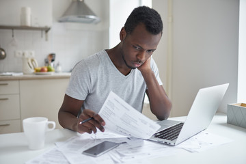 Single young african american male with many debts feeling stressed, calculating finances, siting...