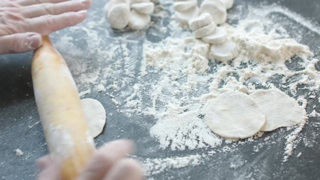Side view of two woman's hands making meat dumpling with wooden rolling pin.
