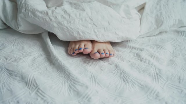 Girl's legs lying in white blanket.