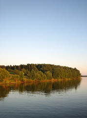 Naklejka na ściany i meble Green autumnal forest near river on blue sky background, vertical view.