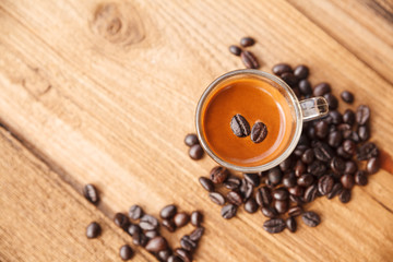 Cup of hot espresso coffee with dark coffee beans on wooden table.