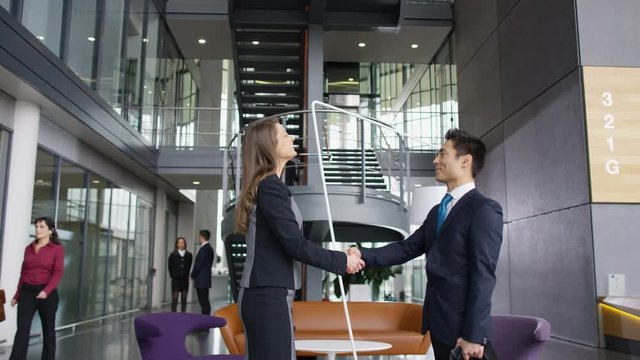  Business people meet & shake hands in large modern office building