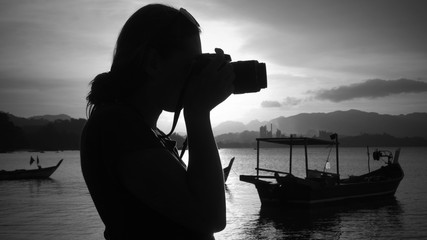 Woman taking a photo with a DSLR digital camera of the beach during sunset in tropical Langkawi island, Malaysia
