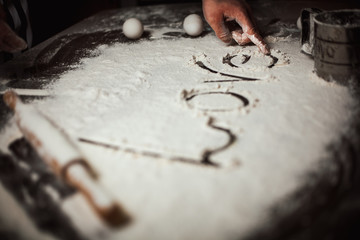 Fototapeta na wymiar A man prepares from flour and writes a finger with the word love on the table