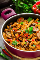 Mediterranean eggplant pasta in pot with tomatoes, red pepper and parsley on grey background.