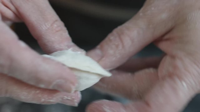 Close-up view of two woman's hands making meat dumplings.