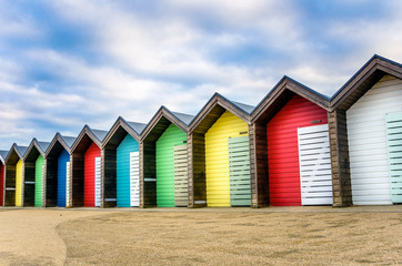 Fototapeta na wymiar Row of Colourful Beach Huts under Blue Sky with Clouds