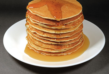 Pile of Fresh Homemade Pancakes Served with Maple Syrup on White Plate, Isolated on Black Background