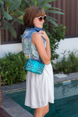 Young stylish woman in trendy outfit with snakeskin python luxury bag in hands. Woman with handbag near the swimming pool.