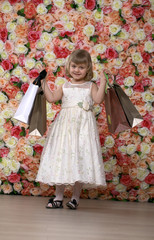 Portrait of a beautiful blonde little girl in white gown with purchases in hands