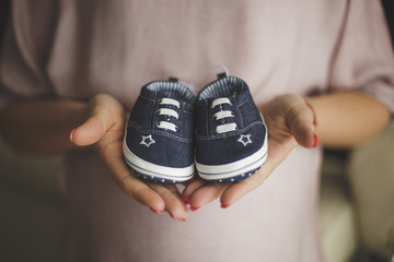 Pregnant woman holding pair of  shoes - obrazy, fototapety, plakaty