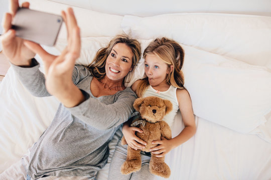 Mother and daughter lying on bed and taking selfie