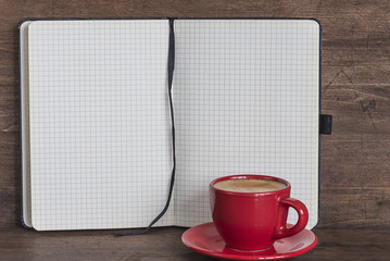 opened copybook and red cup of coffee on wooden background