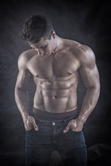 Obraz na płótnie Canvas Handsome young muscular man shirtless wearing jeans, on dark background in studio shot
