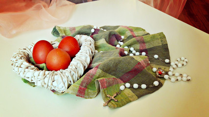 Colored eggs in a white wicker heart and a rosary on the checkered cloth.
