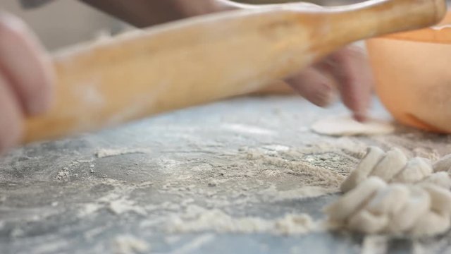 Side view of two woman's hands making meat dumpling with wooden rolling pin.