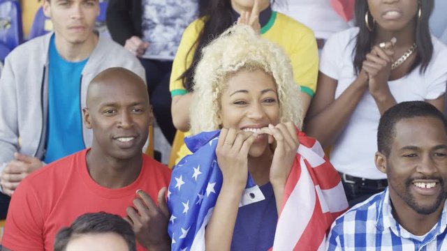  Crowd cheering on their team at sports event, woman holding US flag
