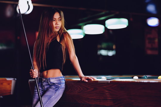 Young beautiful girl in a billiard club, with cue stick posing