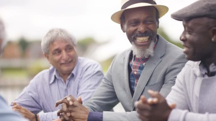  Happy senior male friends chatting & laughing together outdoors in the park - Powered by Adobe