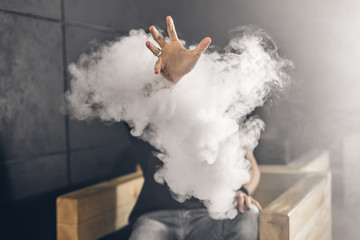 Smoke sticks out of the smoke. Man is vaping in the dark room
